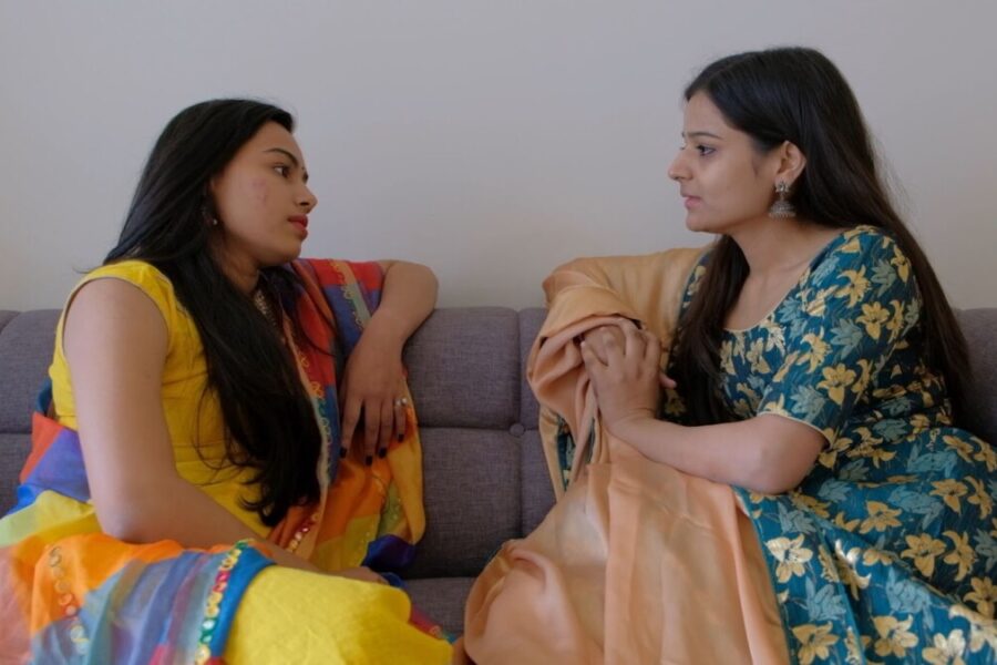 two women facing each other on a couch with serious expressions